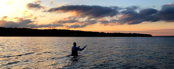 silhouette of a fisherman fly casting into a sunset