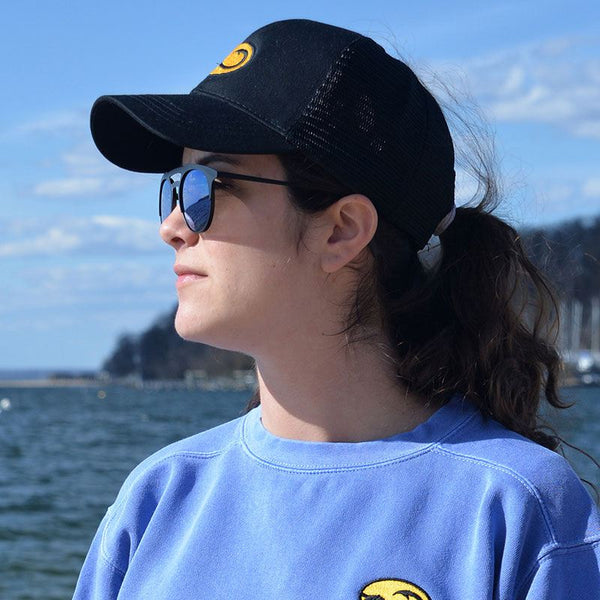 young woman in black Anglers Pride Tugboat Trucker fishing cap at a marina