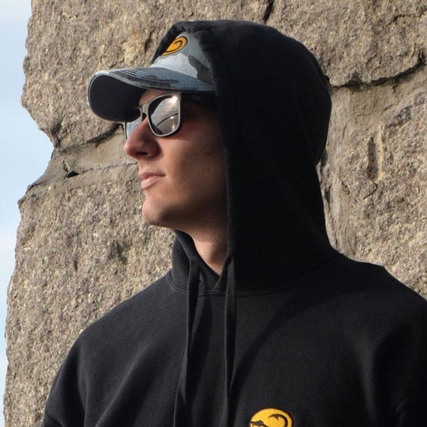 young man in Water Camo fishing cap by Hook Life on sea wall